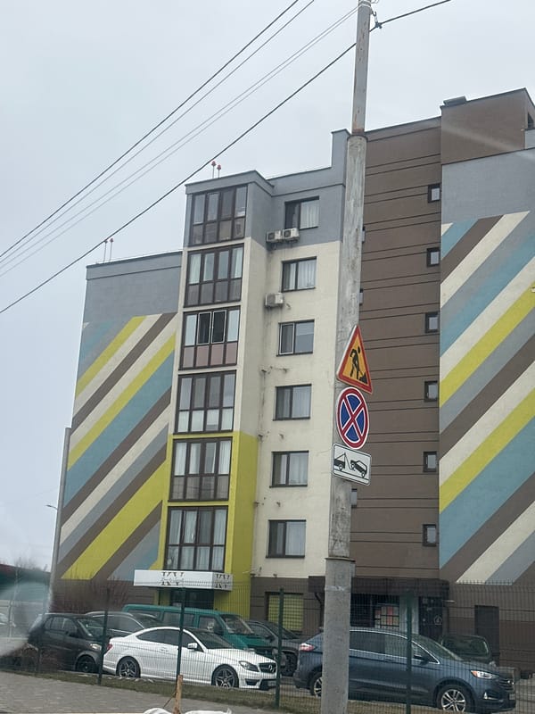 Woman cycles past apartment building in early morning Kyiv