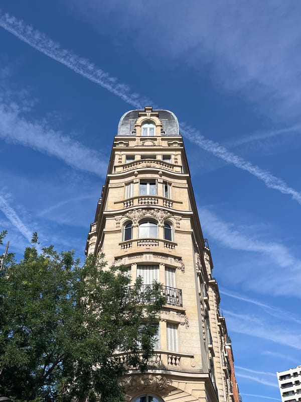 Paris street corner: ornate facades, blue skies, scooter outside a bakery