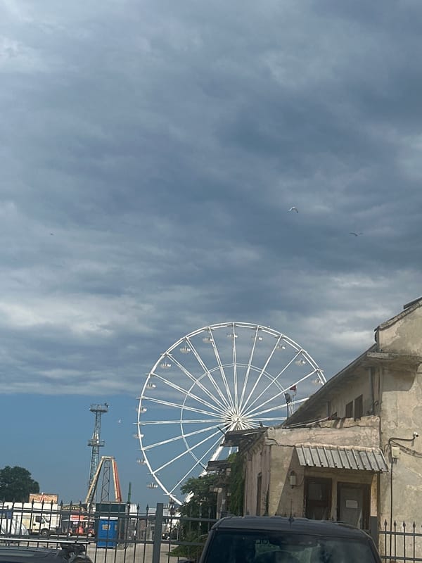 Derelict Ferris wheel beside a working port under stormy skies