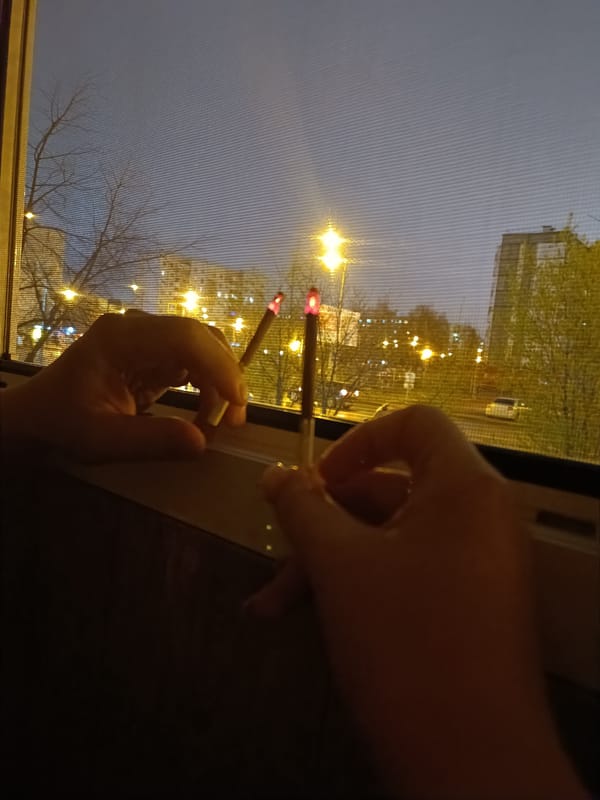 Two people smoke by window in Tobolsk nighttime scene