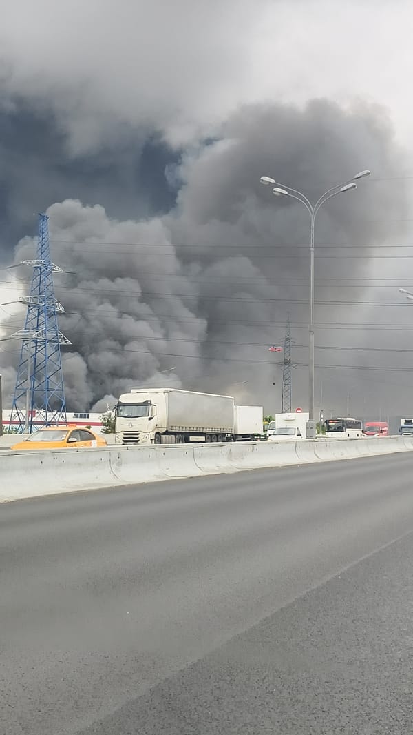 Dark smoke plume rises near industrial area, halting highway traffic