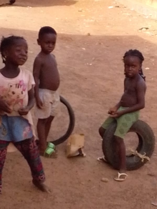 Three children gather, one sitting on tire