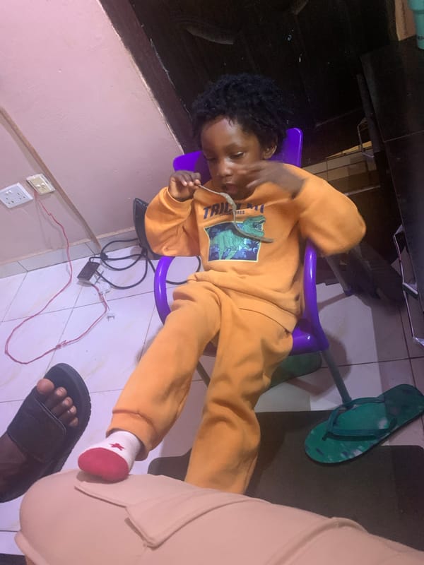 Child in dinosaur sweatsuit relaxes in purple chair, Nigeria
