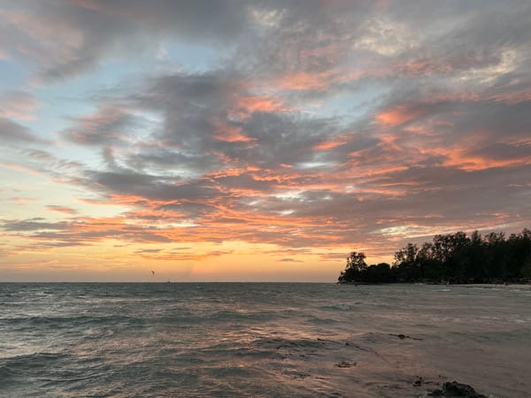 Sunset along a rocky Ko Pha-ngan shoreline, kitesurfer in the mix