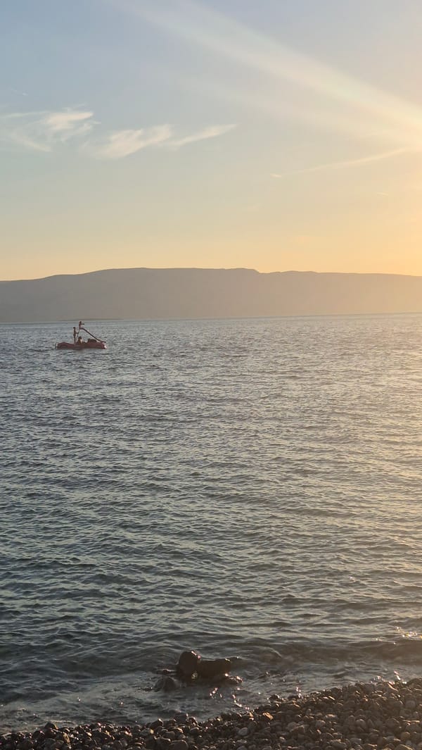 Red boat on calm water, misty mountains glowing in the distance