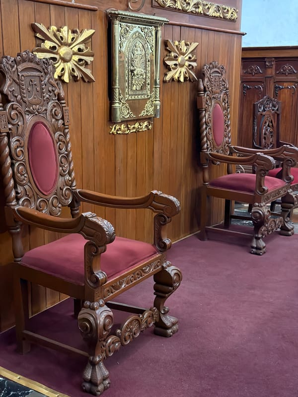 Ornate carved wooden chairs with red cushions documented indoors