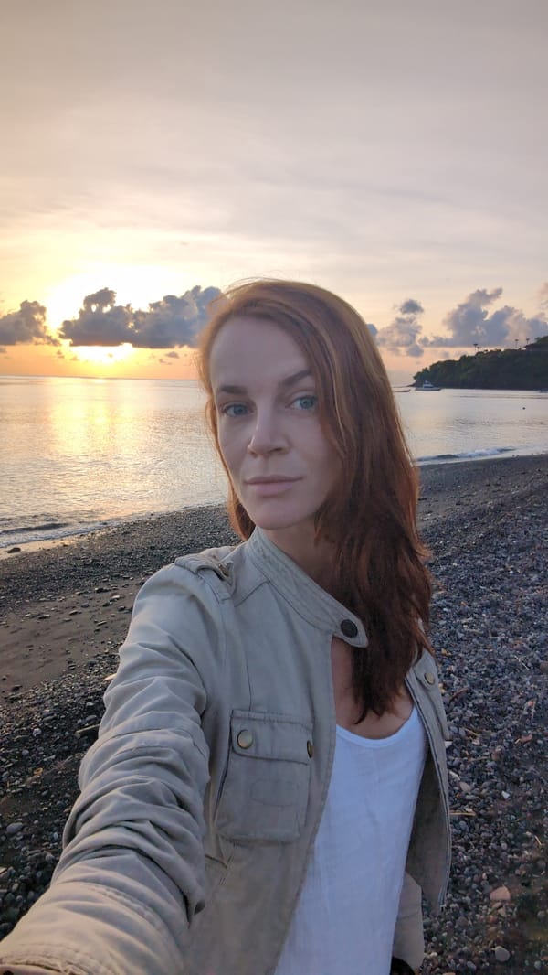 Woman photographs sunset at rocky beach in Abang, Indonesia