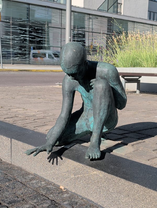 Contemplative bronze sculpture seated on a concrete curb, Stockholm