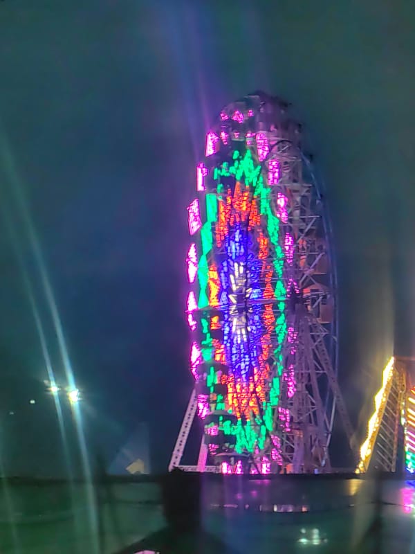 Colorful ferris wheel lights up a rainy night near Pune