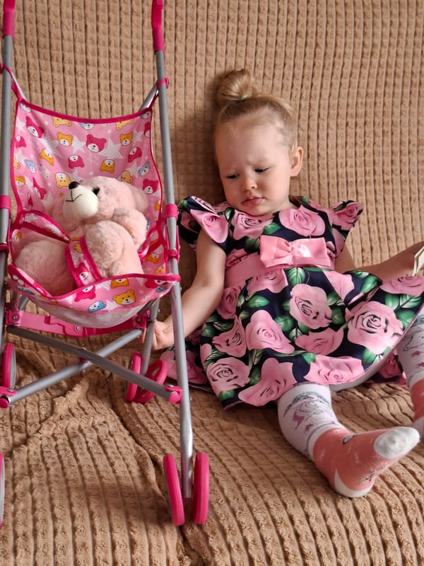 Child plays with toy stroller and teddy bear