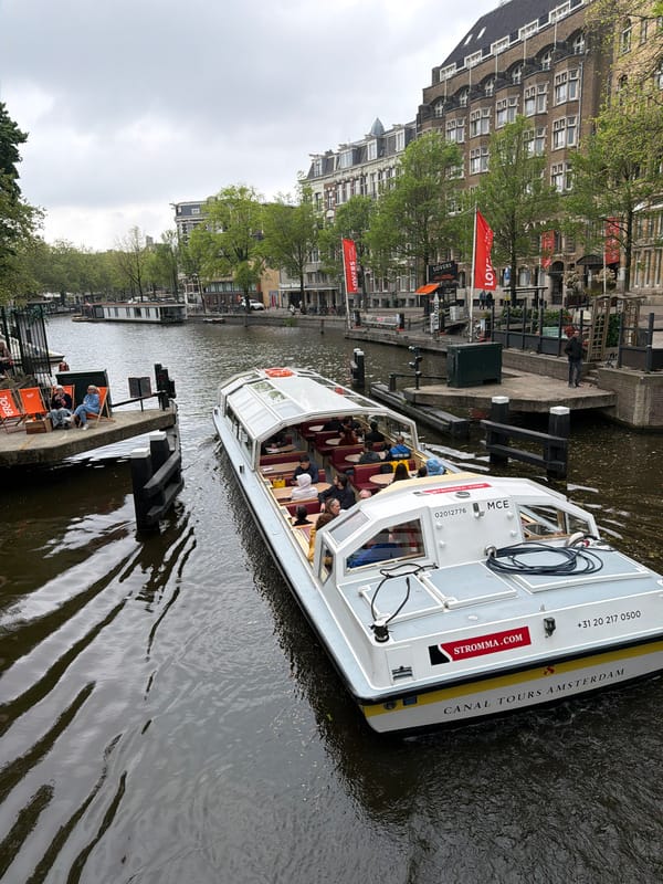 Tourist boat navigates Amsterdam canals past waterfront dining area