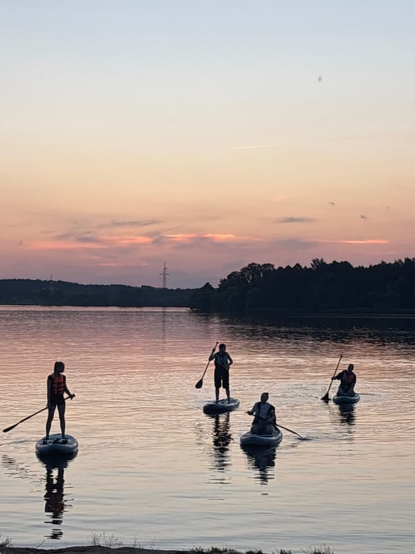 Golden-hour lake scene with paddleboards, pedal boats, and a slow sunset