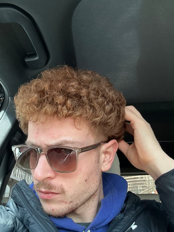 Man in sunglasses sits in car touching hair