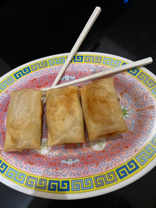 Home-cooked spread: spring rolls, stir-fried greens, and a curious cat