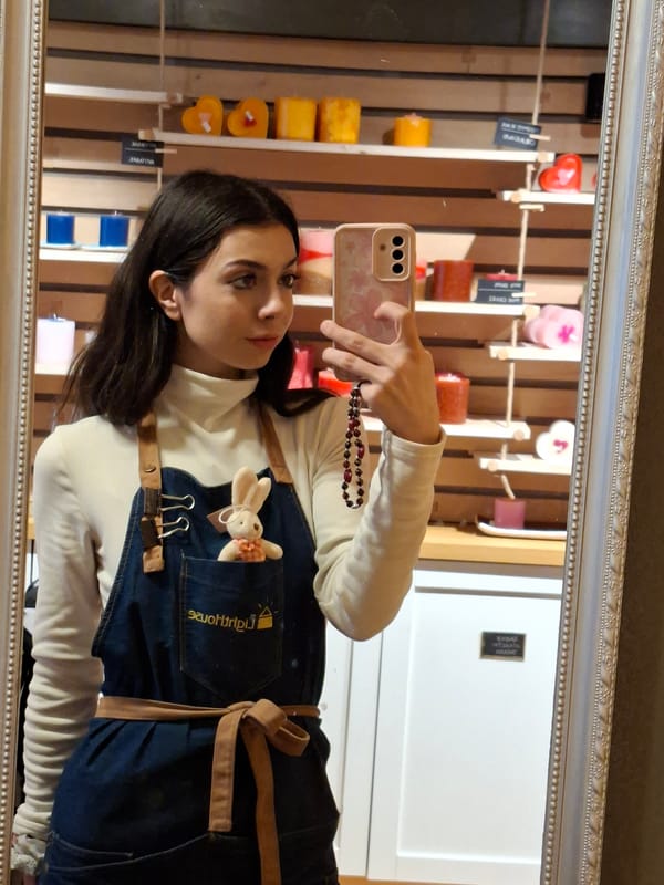 Woman poses in mirror wearing white sweater, denim apron