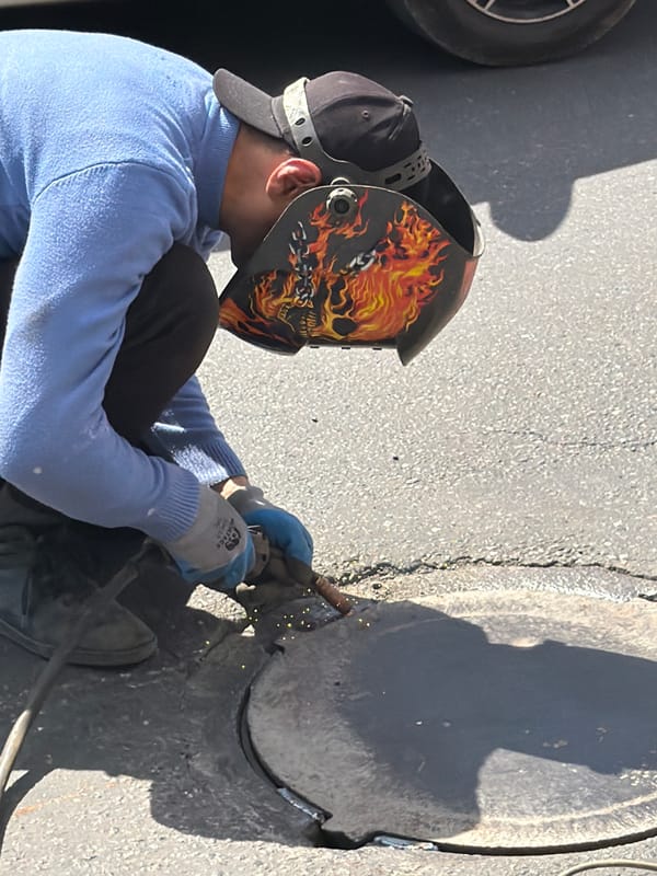Workers conduct outdoor metalwork on rusted plate in Yerevan