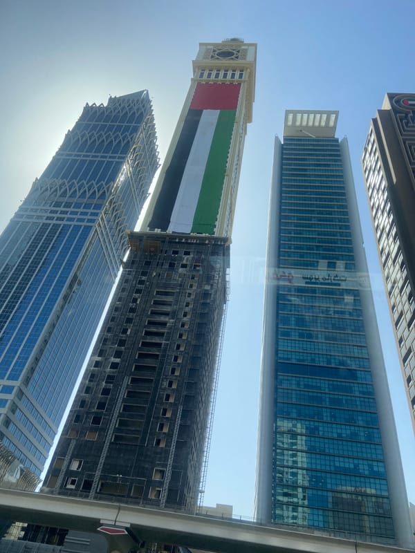Dubai skyscrapers display UAE flag against clear morning sky