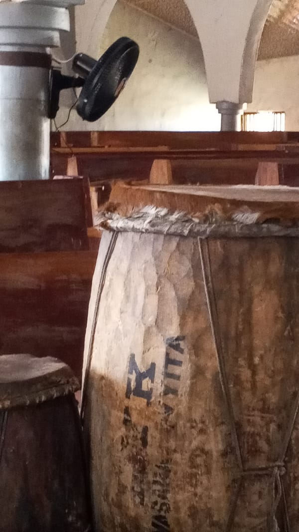 Inside a worship or community hall with drums and wooden pews