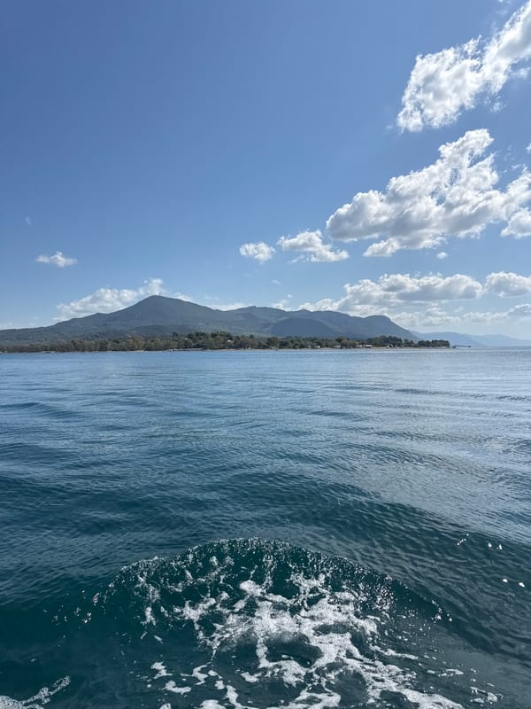 Boat cuts through calm Greek waters toward a wooded island