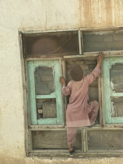Youth climbs through broken window in Kandahar neighborhood