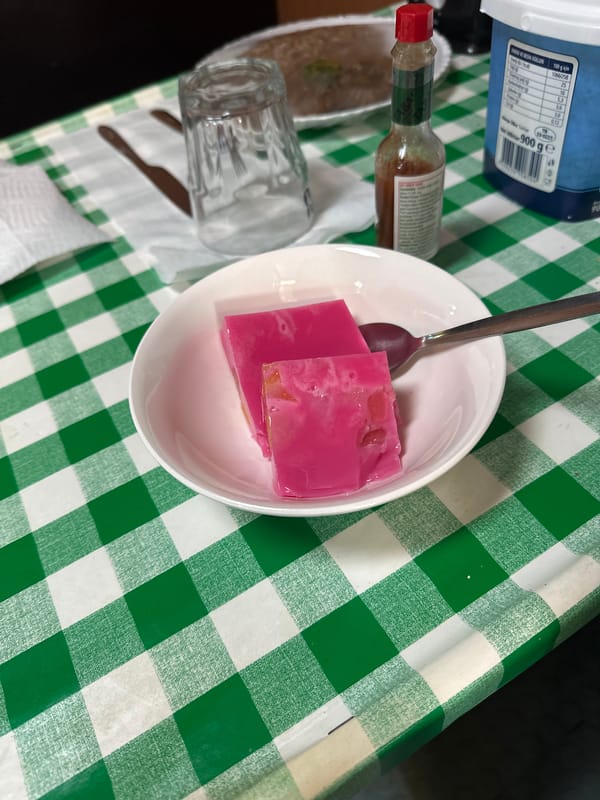 Pink gelatin dessert served in white bowl on checkered surface