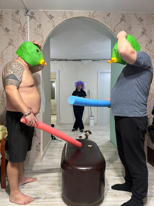 Person in green bird mask holds pink object indoors