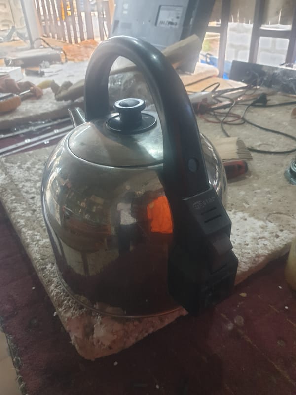Silver kettle photographed on cluttered surface amid household items