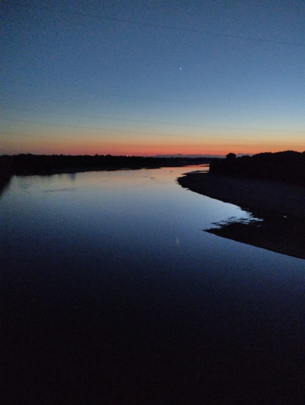 Crane lifts debris from structure near river at dusk