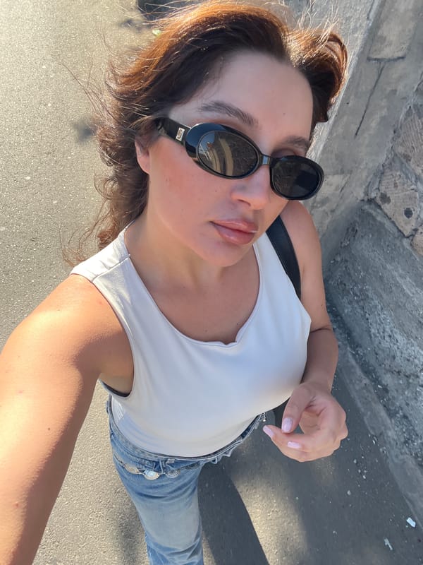 Woman Takes Selfie Near Rose-Covered Building on Sunlit Street