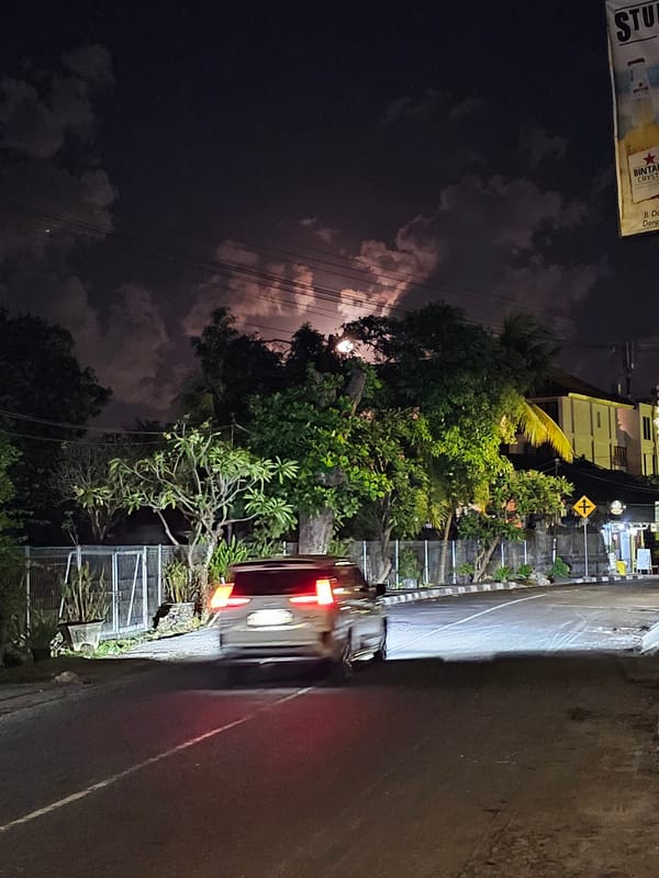 Full moon rising over Denpasar streets, framed by wires and trees