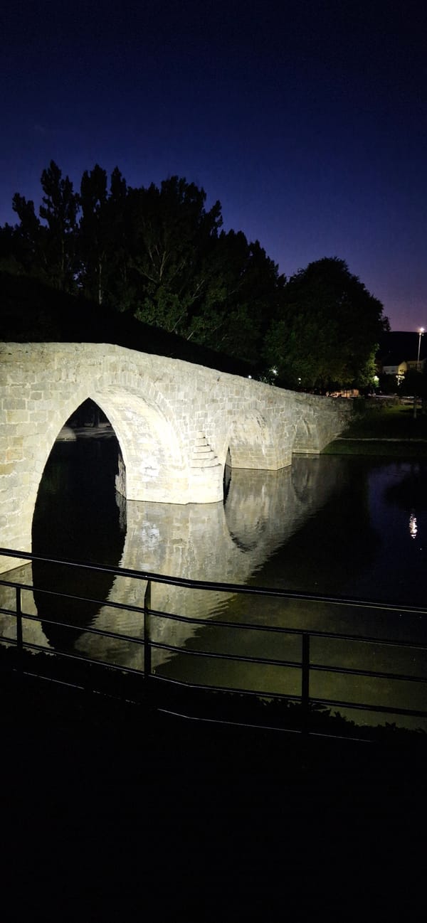 Navaluenga at night: stone bridges, lit pathways, and neon signage