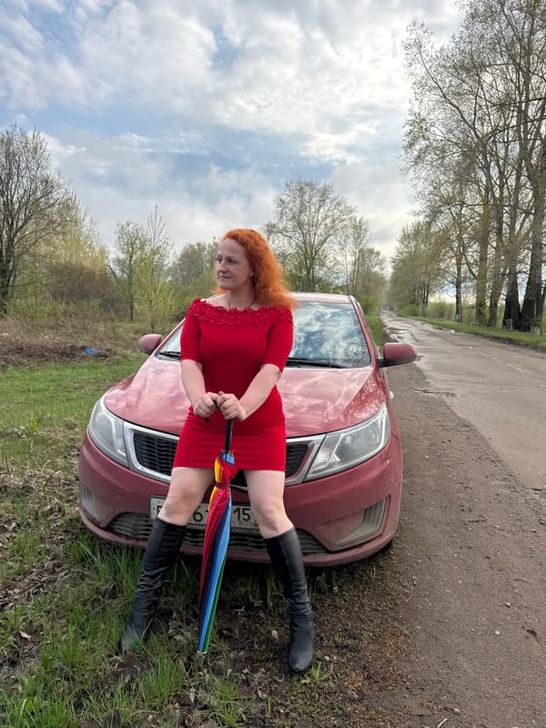 Woman in red poses with rainbow umbrella in rural Russia