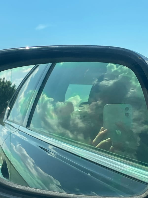 Car mirror reflection captures person with smartphone in Austria