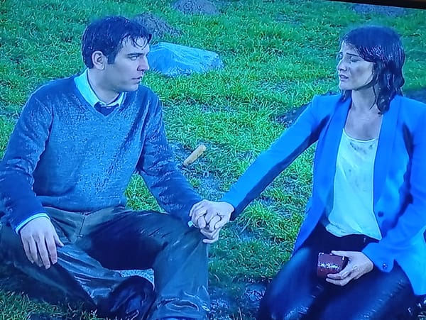 Couple sits in wet grass; coffee machine operated nearby