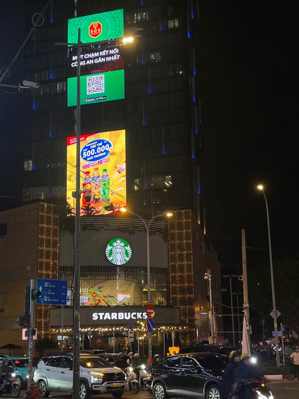 Night traffic flows past illuminated Starbucks in Thủ Đức