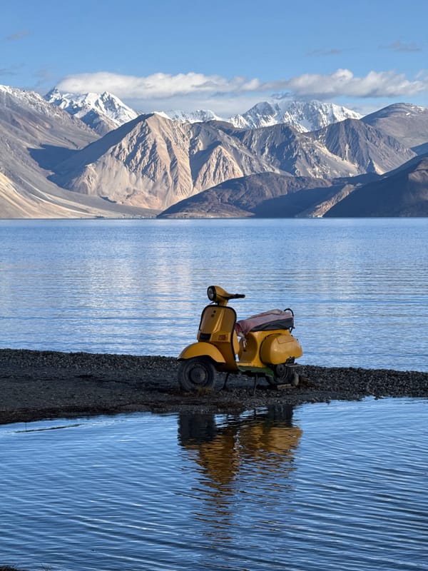 Yellow scooter parked by a calm Ladakhi mountain lake