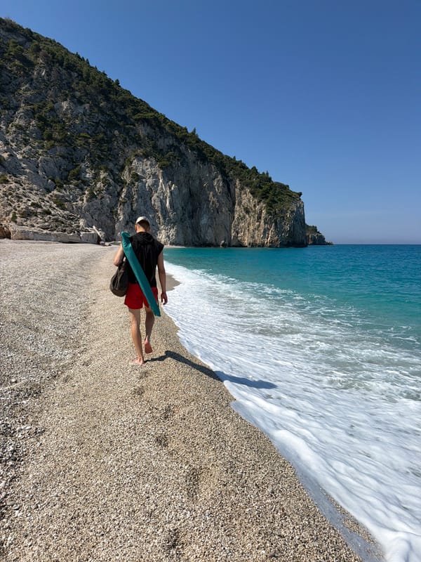 Man walks barefoot on Lefkada beach near limestone cliffs