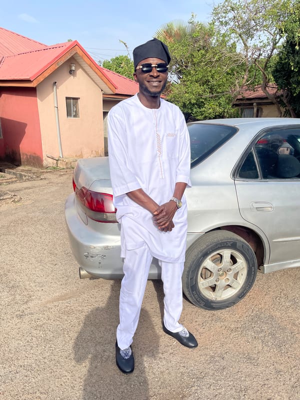 Man in traditional dress poses with silver car