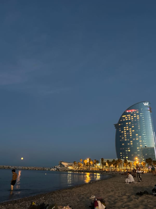 Full moon rises over Barcelona's calm waterfront at twilight