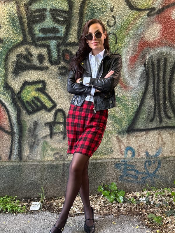 Woman in plaid skirt rests against graffitied wall in Pleven