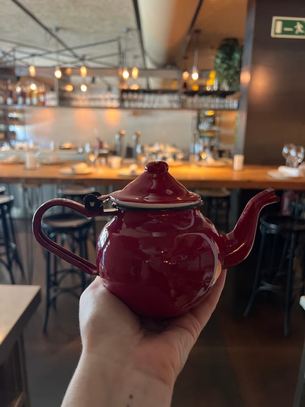 Dark red teapot held up against a Barcelona bar backdrop