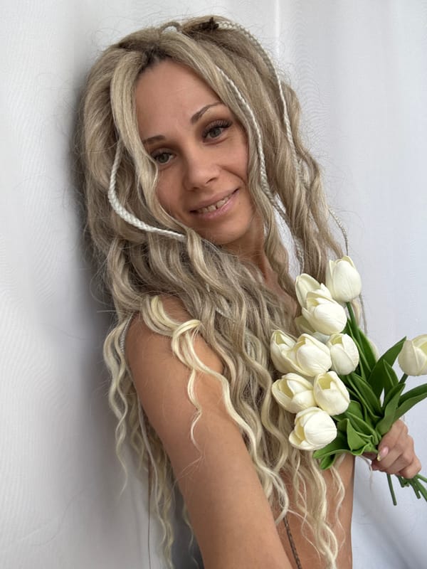 Blonde woman photographed with flowers on white surface