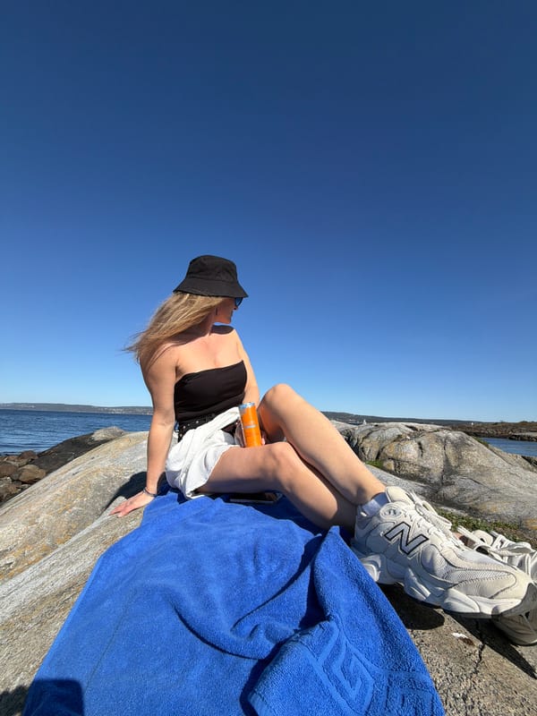 Person relaxes on Norwegian coast as sailboat drifts nearby