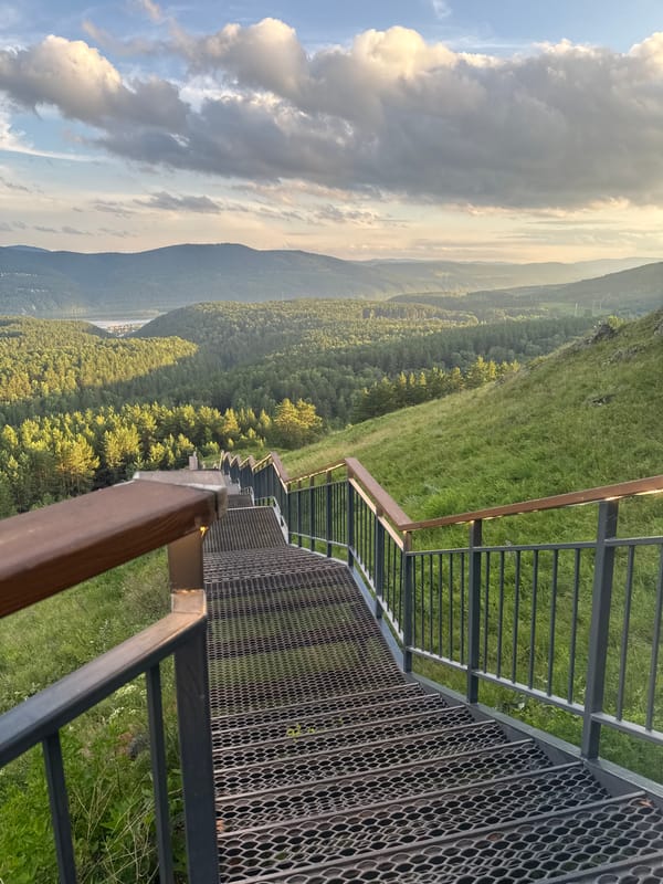 Metal staircase descends a hillside overlooking a wide Siberian valley.