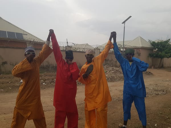 Four robed figures gather, walk dirt path outdoors