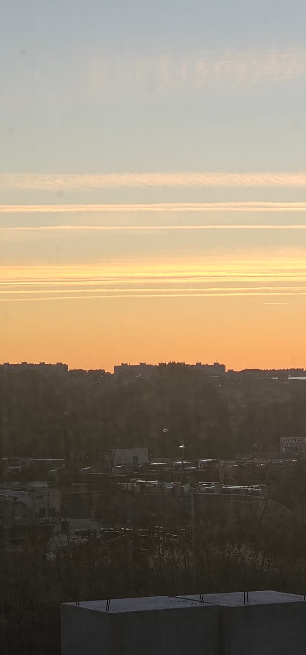 City skyline at dusk, contrails and soft gradients across the sky