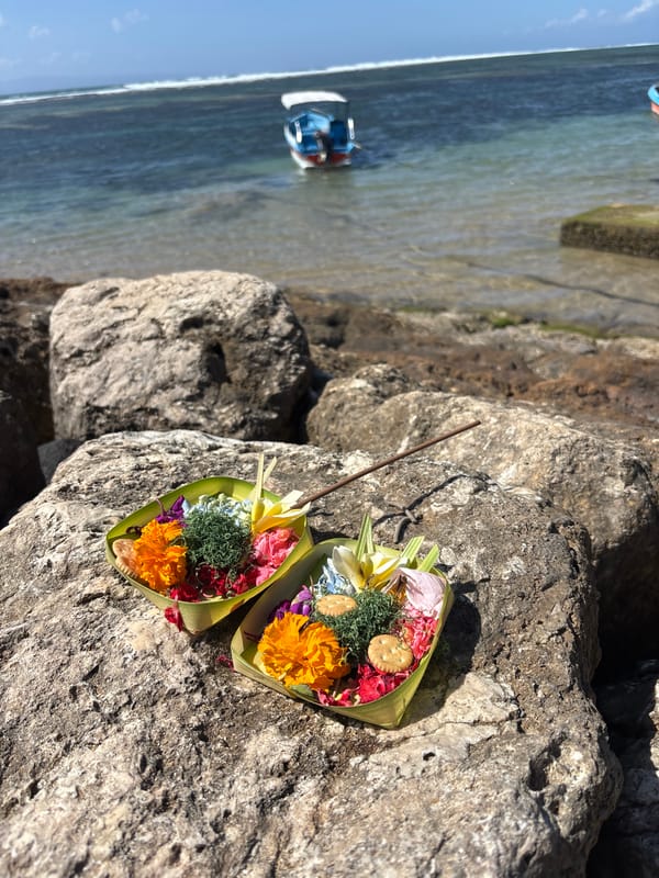 Balinese offerings and fishing boats along a calm Denpasar shore