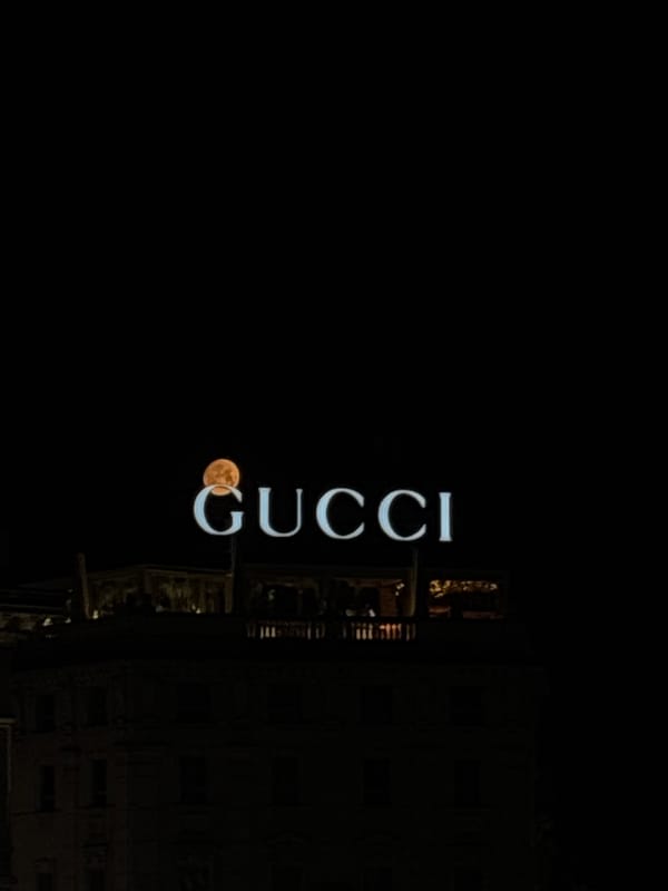 Gucci sign and full orange moon align over Milan night sky