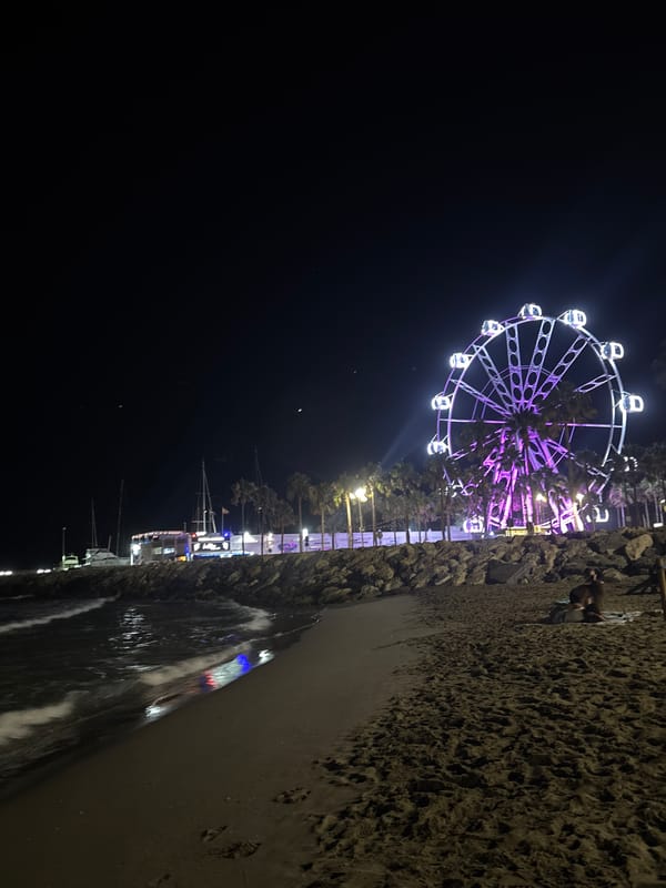 Nighttime beach scene anchored by a glowing Ferris wheel