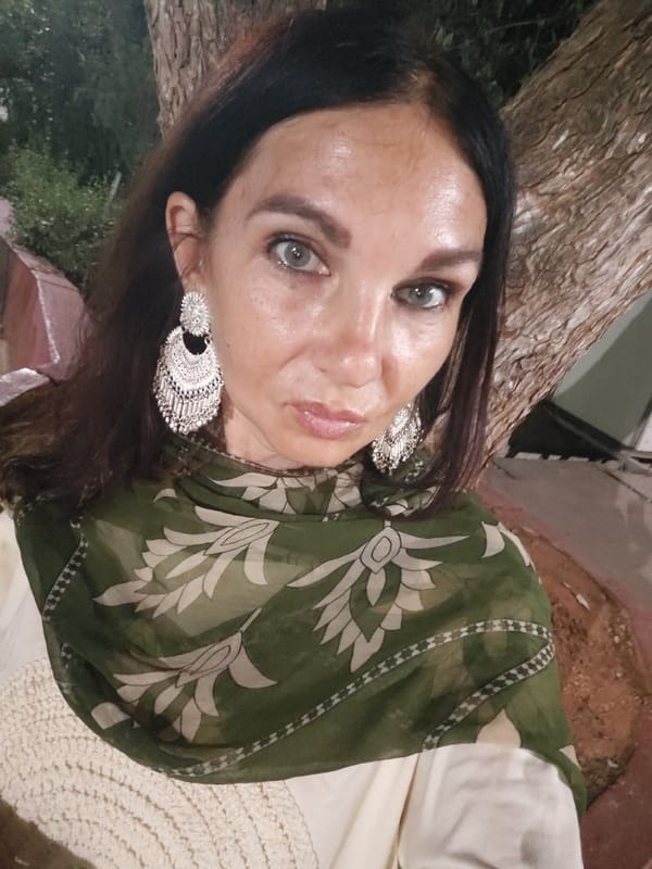 Woman applies makeup, walks among flowering plants in Puttaparthi